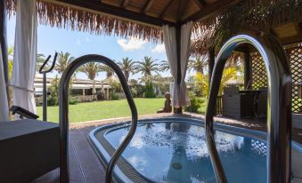 a backyard with a hot tub surrounded by grass , and a swimming pool in the background at Hotel Simius Playa