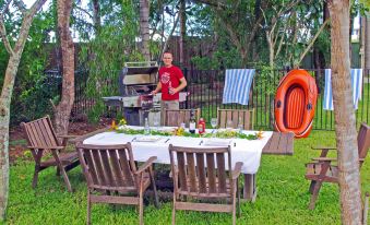 a man wearing a red shirt is cooking on an outdoor grill , surrounded by tables and chairs at Emeraldene Inn & Eco-Lodge