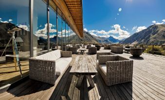 a wooden deck with a dining table , chairs , and couches , surrounded by mountains and overlooking a beautiful landscape at Rooms Hotel Kazbegi