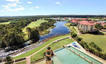 a resort with a large pool , grassy area , and buildings overlooking a body of water at Pelican Waters Resort