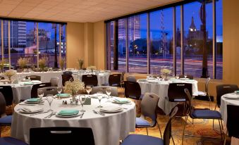 a well - lit dining room with multiple tables set for a formal dinner , each table adorned with blue napkins and green napkins at Aloft Milwaukee Downtown