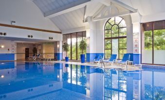 a large swimming pool with blue tiles and a white ceiling , surrounded by lounge chairs at Holiday Inn Glasgow - East Kilbride