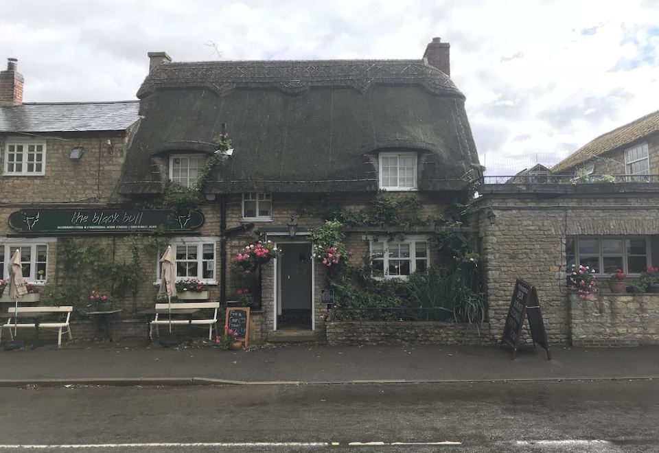 a quaint , thatched - roof building with flowers on the roof , situated on a street corner in a town at The Black Bull