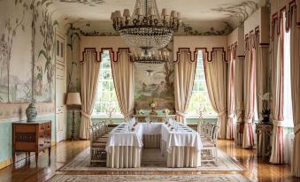 a luxurious dining room with a large table surrounded by chairs , a chandelier hanging from the ceiling , and multiple paintings on the walls at Valverde Sintra Palacio de Seteais