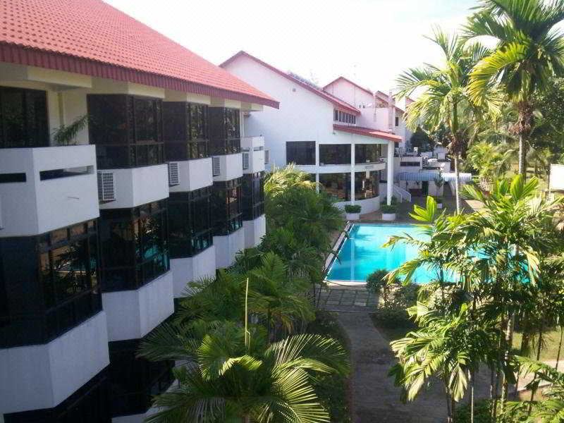 a modern , white building with red roof and multiple balconies , surrounded by lush greenery and a swimming pool at De Rhu Beach Resort