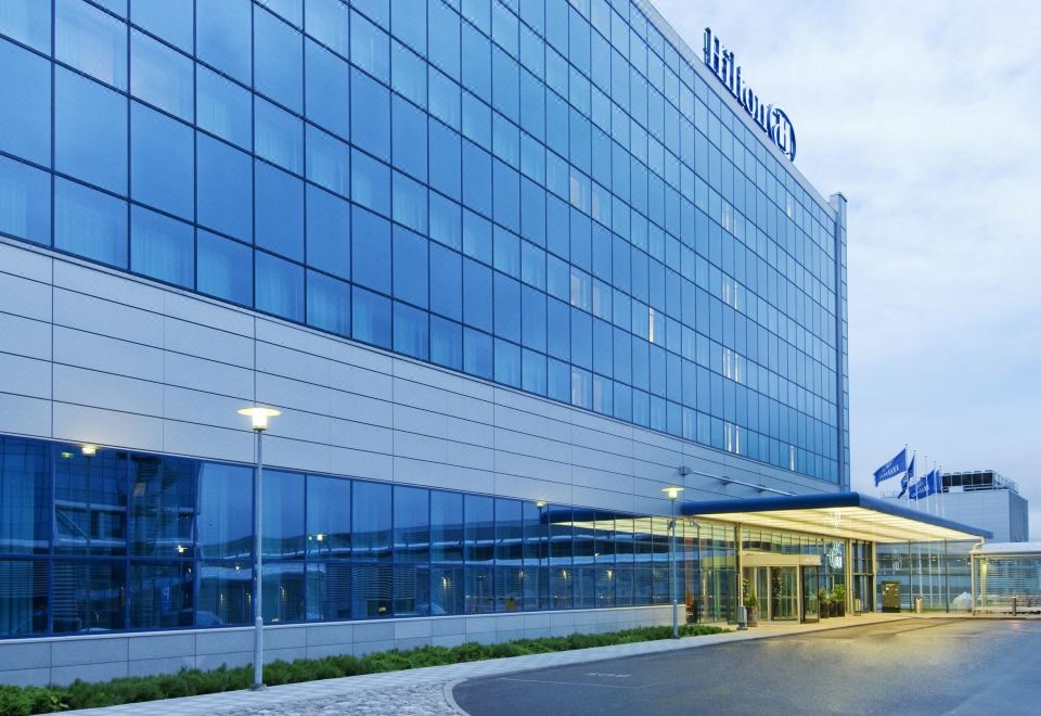 "a large glass building with a sign that reads "" hilton "" prominently displayed on the front of the building" at Hilton Helsinki Airport