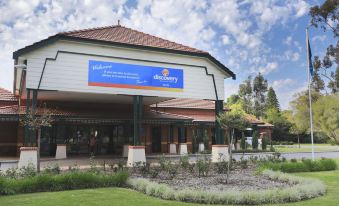 a large white building with a blue banner on the side , situated in a grassy area at Discovery Parks - Perth Airport