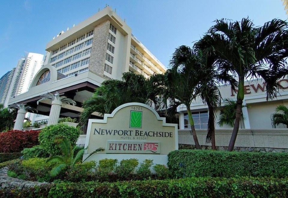 the newport beachside hotel in florida , with its sign and palm trees , under a clear blue sky at Newport Beachside Hotel & Resort