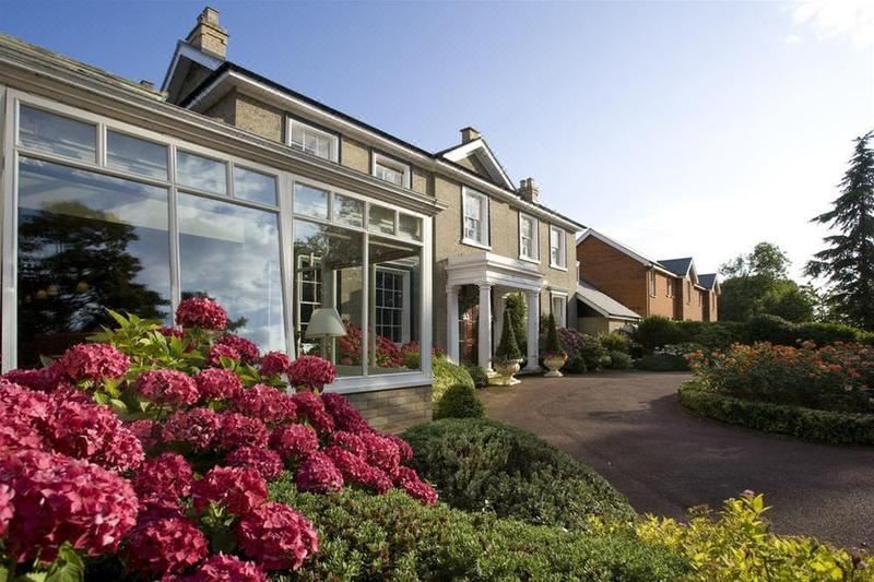 a large , modern house with a red roof and glass windows is surrounded by greenery and flowers at Cbh Park Farm Hotel