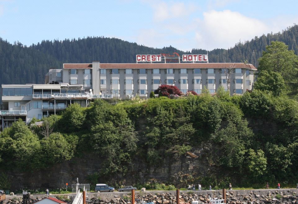 a large hotel building situated on the shore of a body of water , with boats docked nearby at Crest Hotel