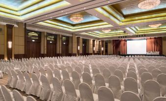 a large , well - lit conference room with rows of white chairs arranged in a symmetrical pattern at Ajman Hotel by Blazon Hotels