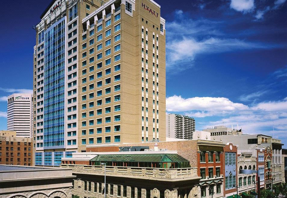a tall , beige - colored hotel with a green roof is surrounded by smaller buildings and people at Hyatt Regency Calgary