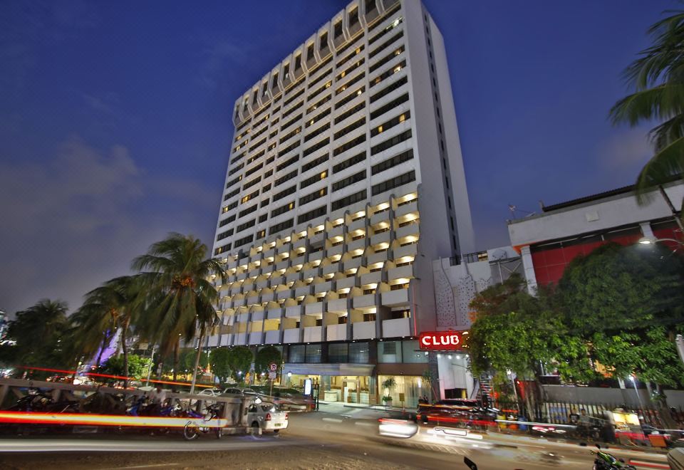 a tall building with a club sign on top is surrounded by palm trees and street lights at Jayakarta Hotel Jakarta