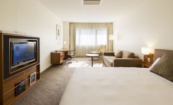 a hotel room with a bed , couch , tv , and window , all decorated in neutral colors at Novotel Canberra