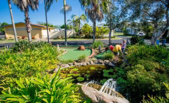 a group of people playing miniature golf on a green field with water fountains in the background at Discovery Parks - Ballina