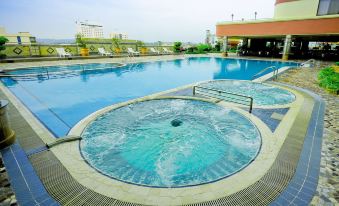 a large outdoor swimming pool surrounded by multiple buildings , with people enjoying their time in the pool at Planet Holiday Hotel & Residence