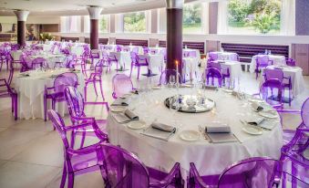 a large dining room with multiple tables covered in white tablecloths and adorned with purple chairs at Hotel Da Vinci