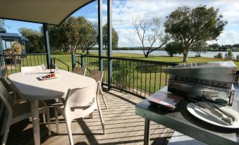 a patio with a table , chairs , and a grill overlooks a lake and trees from a balcony at Discovery Parks - Ballina