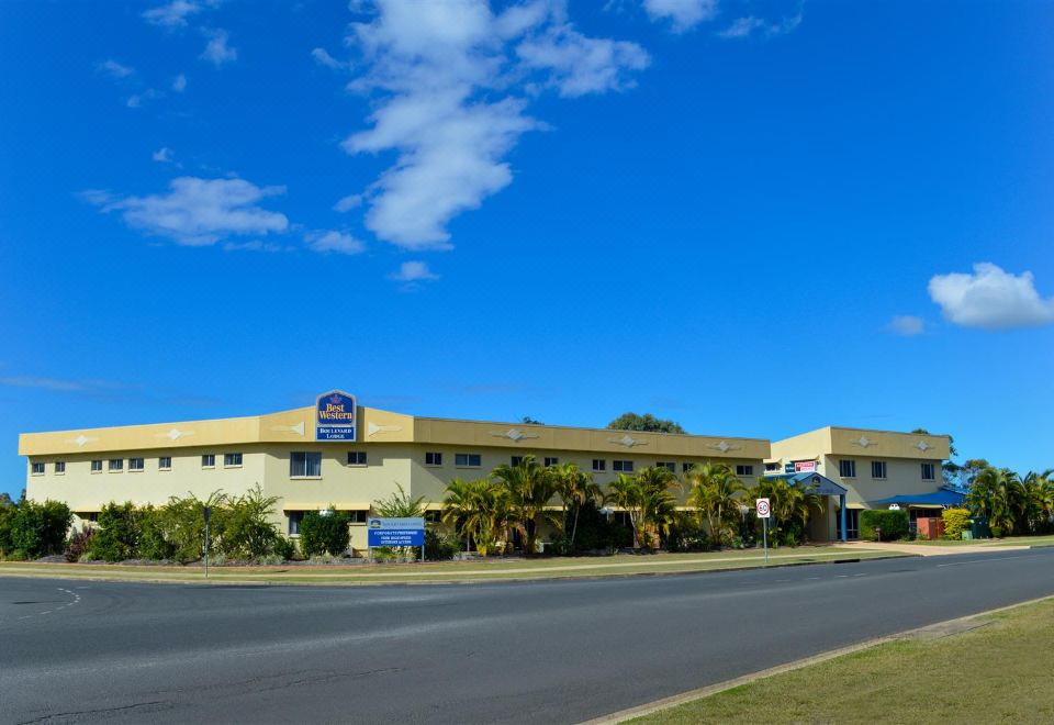 a large building with a blue sign on the side is surrounded by palm trees at Boulevard Lodge Bundaberg