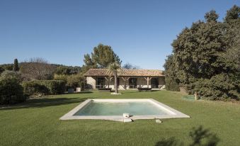 a large , rectangular pool is surrounded by a grassy yard with a house in the background at Domaine la Pierre Blanche
