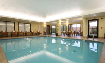 an indoor swimming pool surrounded by tables and chairs , providing a pleasant atmosphere for guests at Courtyard Flint Grand Blanc