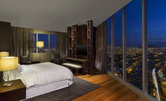 a bedroom with a large bed , wooden floors , and a window overlooking a cityscape at night at The Westin Guadalajara