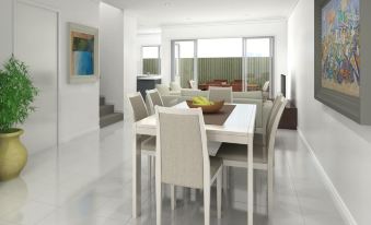 a modern dining room with a large table and chairs , white walls , and a sliding glass door at Direct Collective - Breeze on Brightwater
