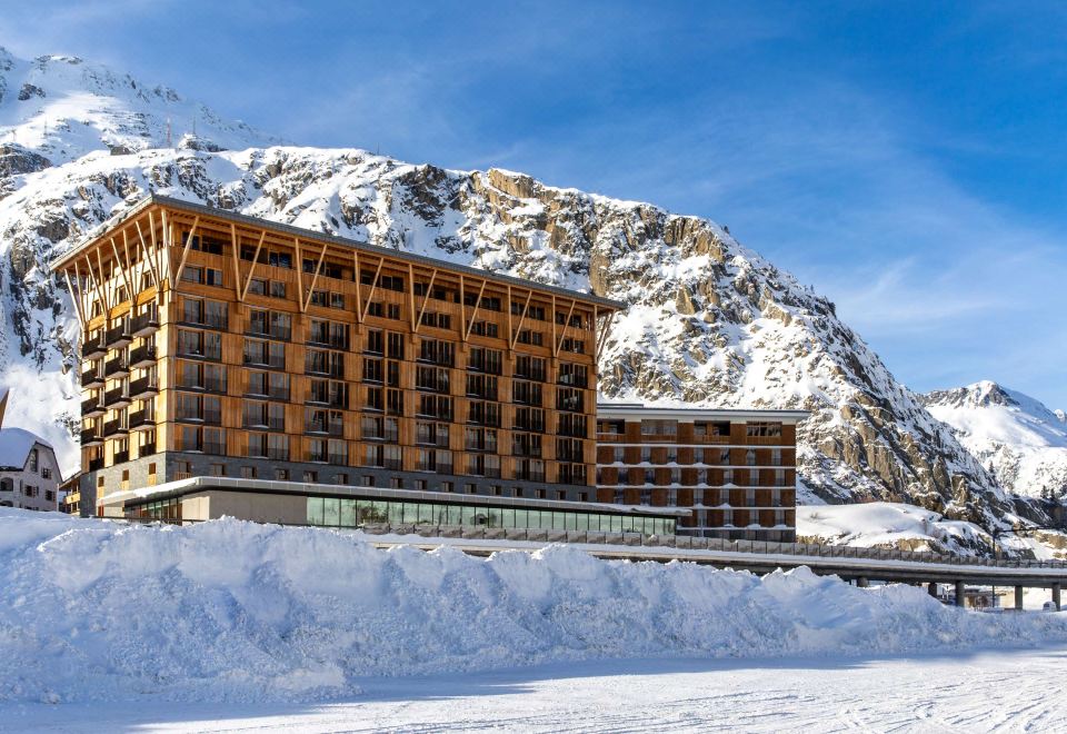 a large building with a wooden facade is situated in front of a snowy mountain at Radisson Blu Hotel Reussen Andermatt