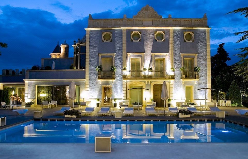 a large villa with a swimming pool in front of it , illuminated by lights at night at Hotel Ferrero - Singular's Hotels