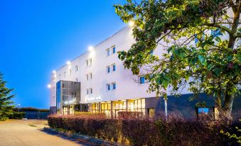 "a large white building with a sign that says "" hotel "" is lit up at night" at Comfort Hotel Aeroport Lyon St Exupery