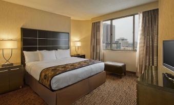 a large bed with white sheets and a brown headboard is in a hotel room with a window at DoubleTree Suites by Hilton Minneapolis