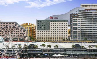a large building with a red sign is surrounded by palm trees and other buildings at Ibis Sydney Darling Harbour