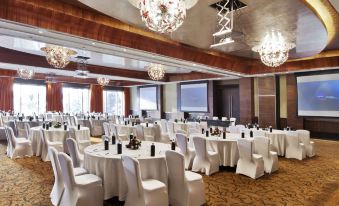 a large conference room with white tables and chairs , chandeliers hanging from the ceiling , and windows at Novotel Mumbai Juhu Beach