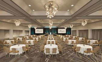 a large conference room with multiple tables and chairs , surrounded by chandeliers and a stage at Fairmont Dallas