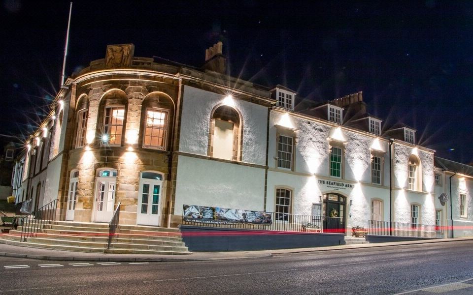 a brick building with a sign on the side , illuminated by street lights at night at The Seafield Arms-Cullen