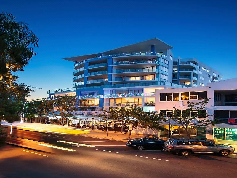 a city street at night , with a tall building in the background and a group of people standing on the sidewalk at Scarborough Beach Resort