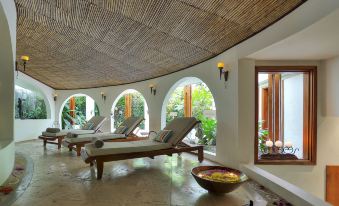 a large , curved room with several wooden lounge chairs and a stone floor is adorned with potted plants at Tabacon Thermal Resort & Spa