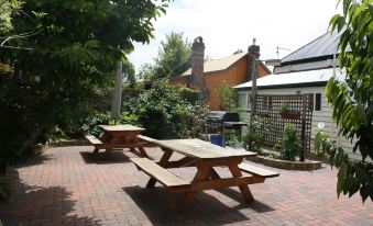 a brick courtyard with two picnic tables and a grill , surrounded by trees and plants at Westbury Gingerbread Cottages