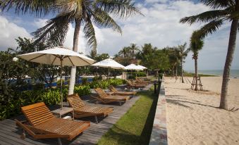 a row of wooden lounge chairs under umbrellas on a sandy beach with palm trees at Kuiburi Hotel & Resort
