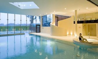 an indoor swimming pool with a person sitting on the edge and a staircase leading up to it at Ockenden Manor Hotel & Spa