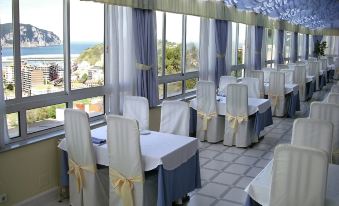 a restaurant with white tables and chairs , blue tablecloths , and a view of the ocean at Hotel Miramar Laredo