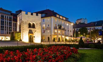 a large building with a restaurant on the ground floor and a flower garden in front at Hotel Post Alpine Cityflair