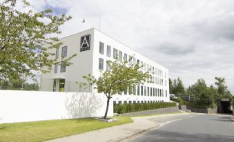 "a large white building with a sign that reads "" aarhus universitet "" is surrounded by trees and a sidewalk" at A Hotels Glostrup