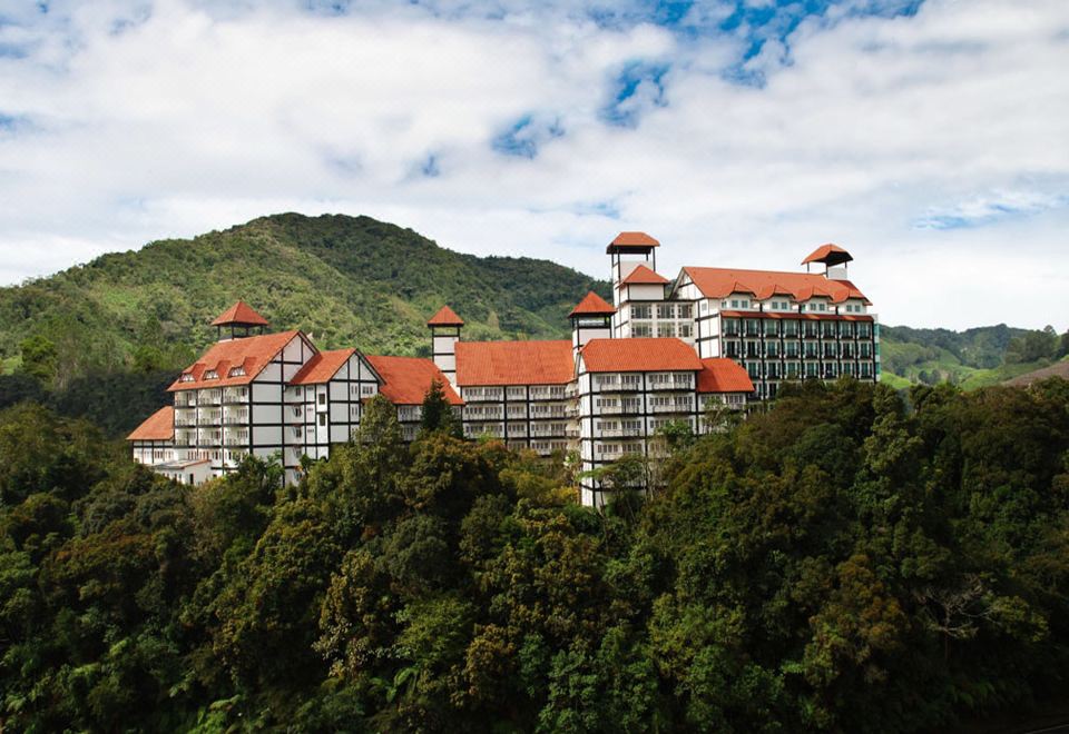 a large , white building with red roofs and multiple towers is perched on a hillside at Heritage Hotel Cameron Highlands