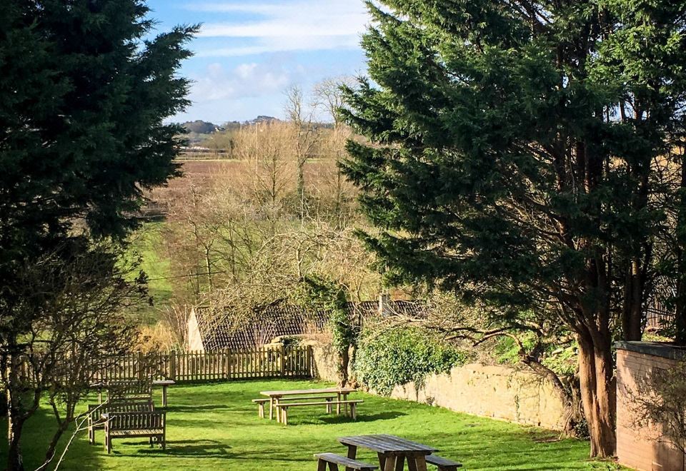 a lush green lawn with several picnic tables and benches , surrounded by trees in the background at The White Hart