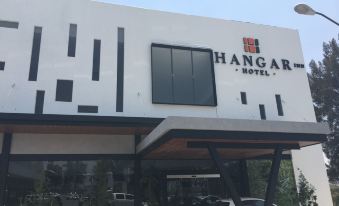 "a white building with a black sign that says "" hangar hotel "" is shown with cars parked in front" at Hangar Inn Guadalajara Aeropuerto