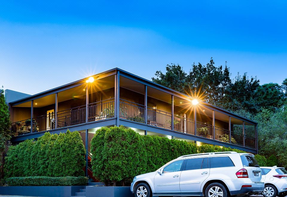 a white car is parked in front of a two - story house with a balcony and greenery at Barkly Motorlodge