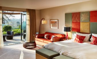 a modern bedroom with a large window , red sofa , and wooden bed , overlooking a balcony at Ockenden Manor Hotel & Spa