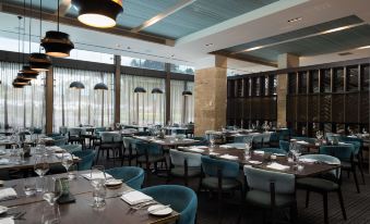 a modern , well - lit restaurant with blue chairs and tables , white tablecloths , and large windows offering views of the outdoors at Rydges Campbelltown an EVT hotel