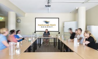 "a group of people sitting at a table in a conference room with a screen displaying "" scarborough beach resort .""." at Scarborough Beach Resort